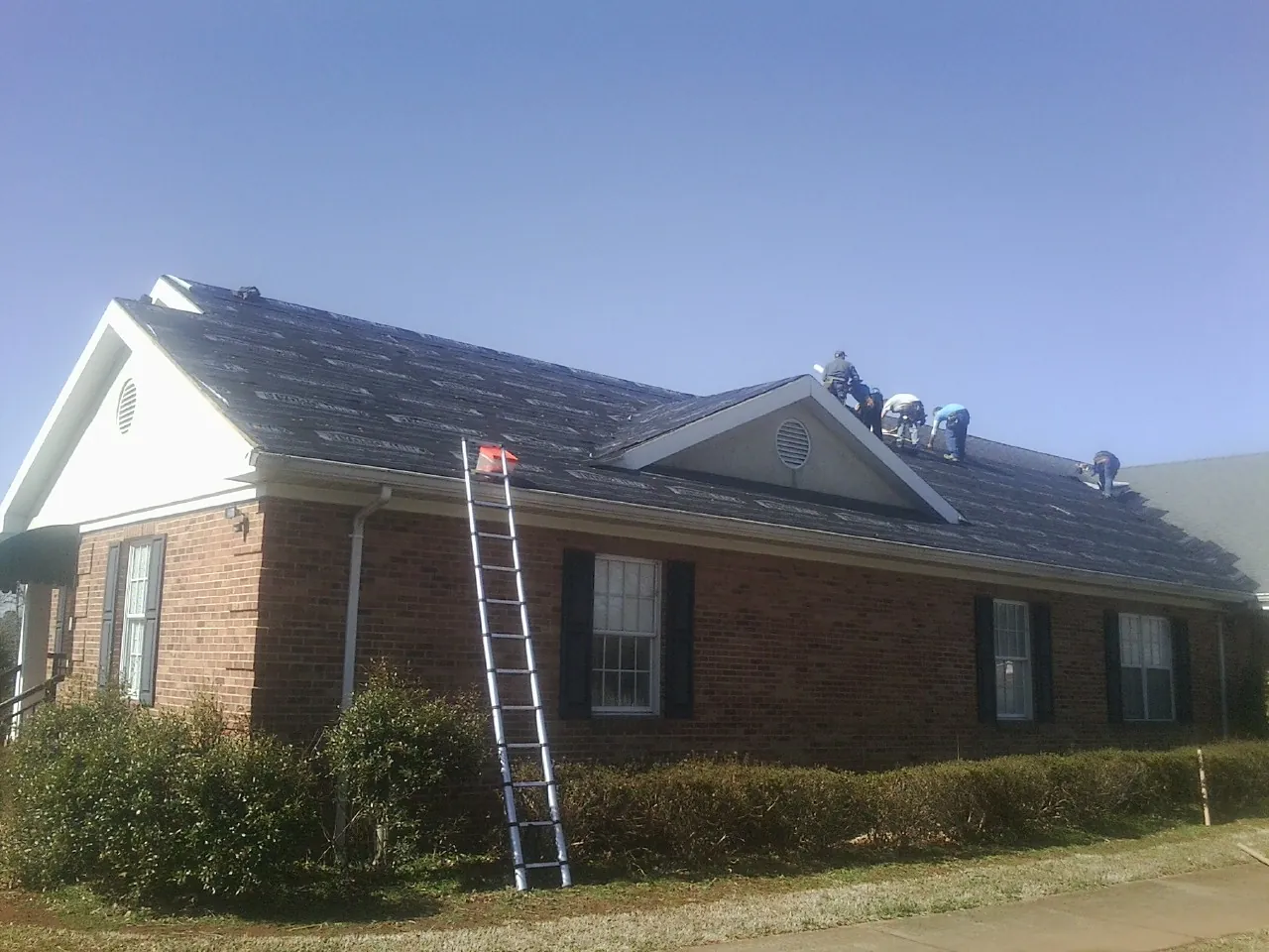 Crew tearing shingles off a brick ranch roof with a ladder set — Emergency Roof Repair work by our crew in Berry