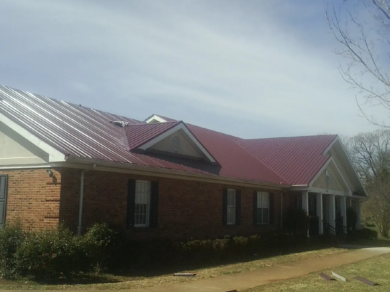 Red metal roof with gabled entries on a long brick building, from a Hail Damage Roof Repair job in Berry