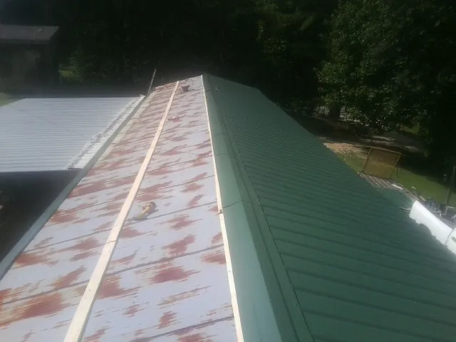 Old rusted panels beside newly installed green metal roofing — Wind Damage Roof Repair by Roofing Brothers in Berry