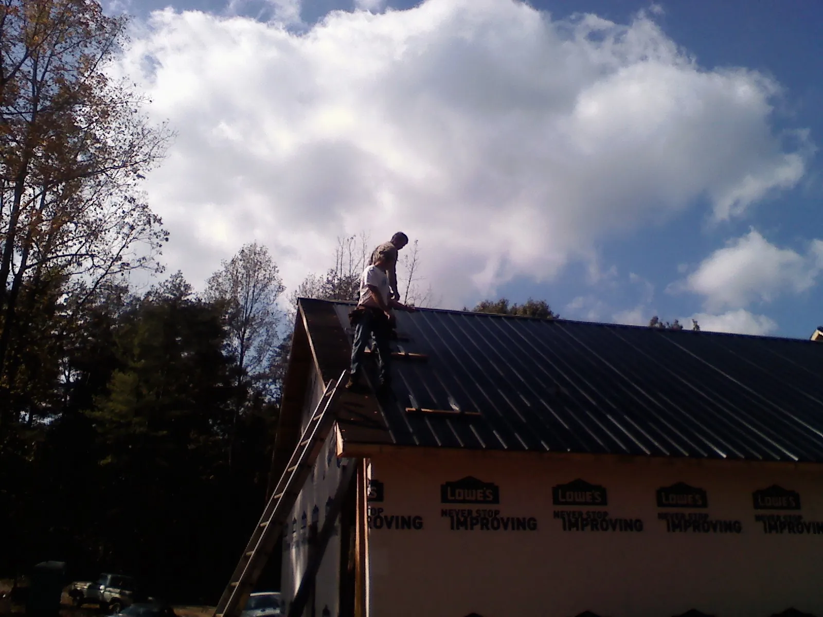Roofer fastening dark metal panels high against a cloudy sky, from a Roof Inspection job in Berry
