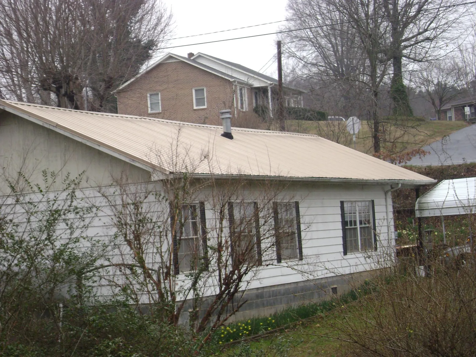 Tan metal roof on a white sided house set into a hillside — Commercial Roofing by Roofing Brothers in Berry